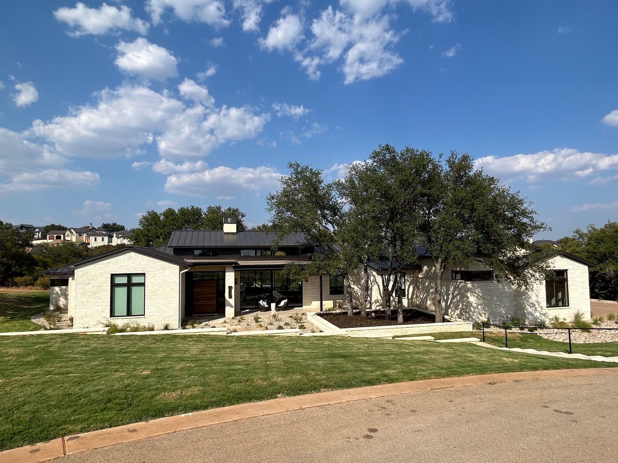 Low, modern home with a flat-roofed center and white limestone wings among live oaks