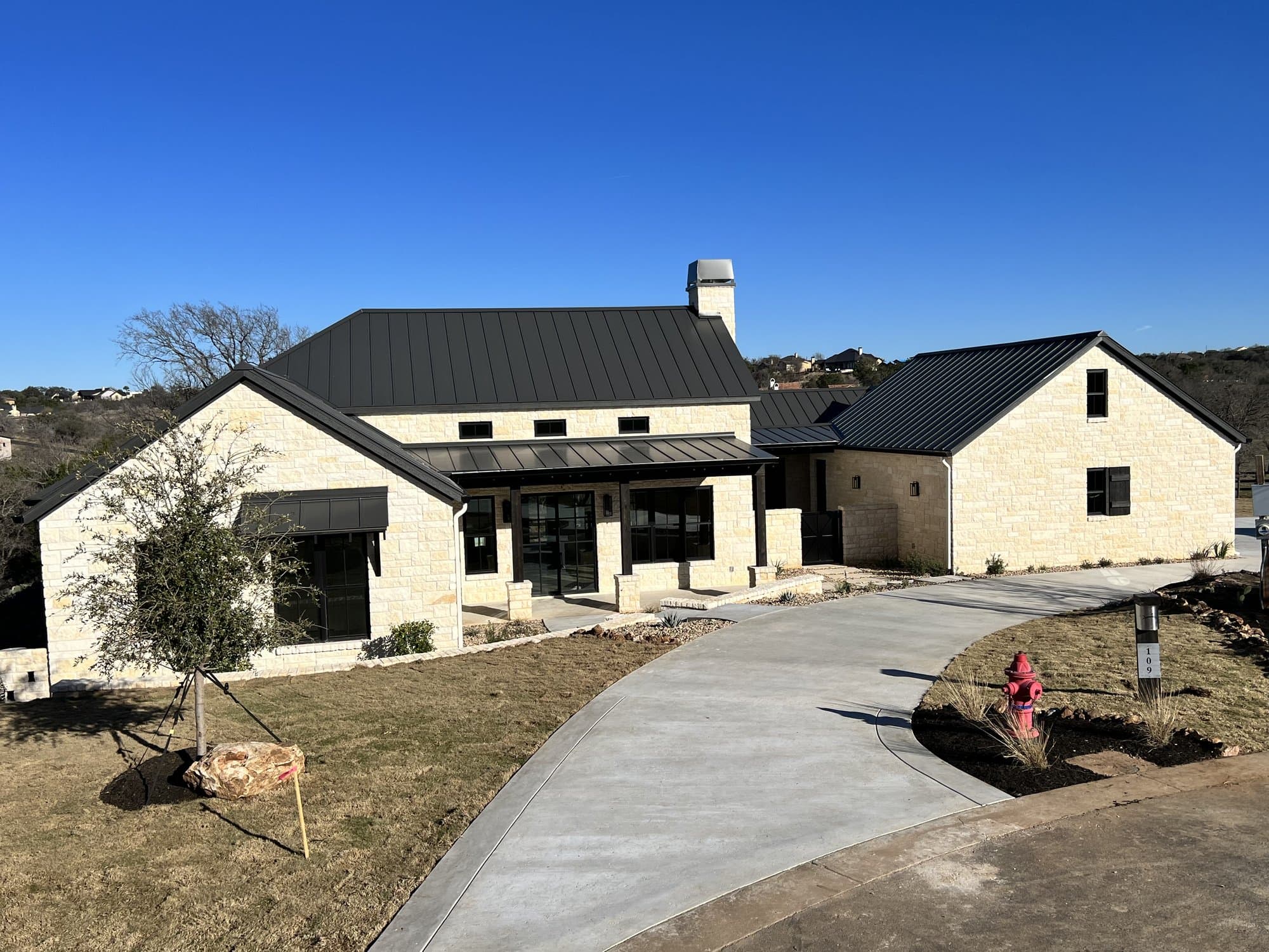 White limestone home with a black metal roof and a curving concrete driveway