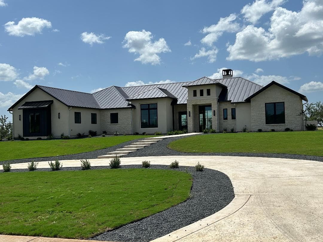 Single-story limestone ranch home with a metal roof behind a wide lawn and curving drive